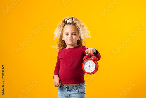 Young girl holding an alarm clock, symbolizing time management, education, school, and the urgency of deadlines and study."