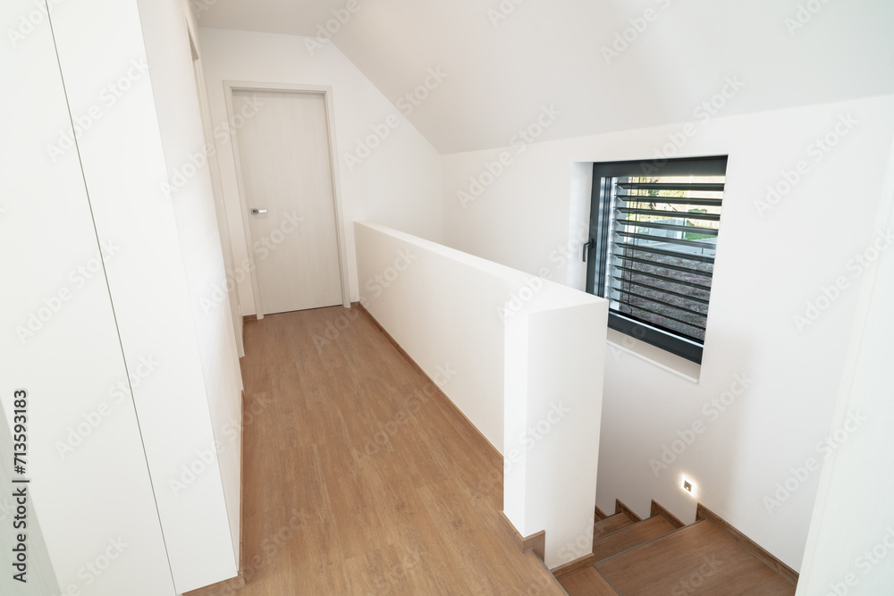 An attic hallway with two sets of stairs and a window. The walls are painted a white color and the floors are made of wooden planks. The hallway has a simple and elegant design. An attic hallway with two sets of stairs and a window. The walls are painted a white color and the floors are made of wooden planks. The hallway has a simple and elegant design.