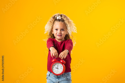 Young girl holding an alarm clock, symbolizing time management, education, school, and the urgency of deadlines and study."