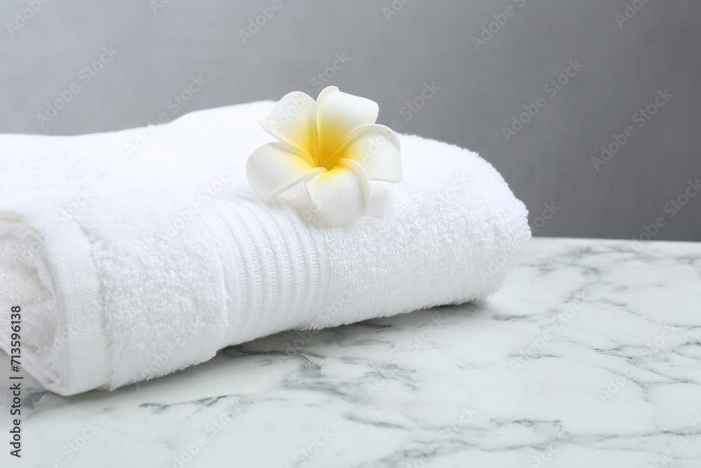 Folded terry towel and plumeria flower on white marble table, closeup. Space for text Folded terry towel and plumeria flower on white marble table, closeup. Space for text