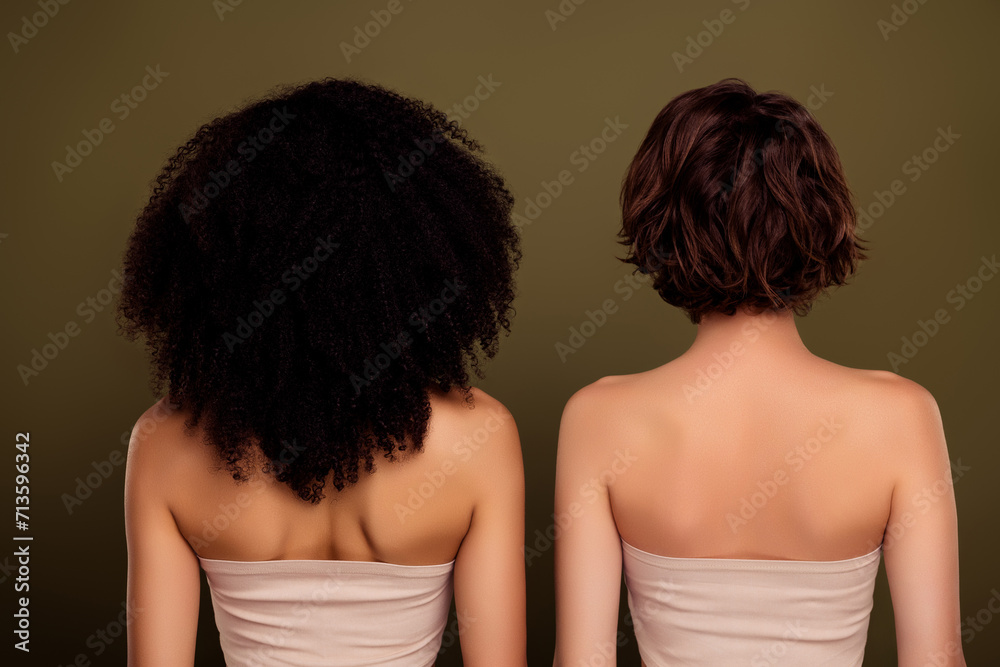 Naklejka premium Rear view of two different ladies with curly american hairstyle vs bob brown haircut isolated on khaki color background