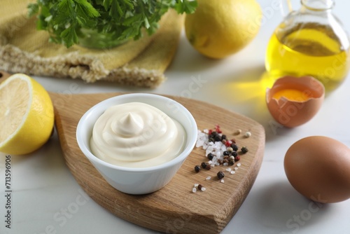 Tasty mayonnaise sauce in bowl, ingredients and spices on white table