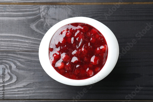 Fresh cranberry sauce in bowl on black wooden table, top view photo