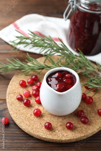 Cranberry sauce in pitcher, fresh berries and rosemary on wooden table