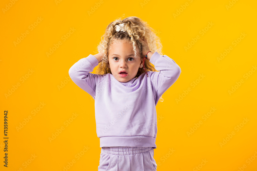 Surprised child girl holding her head on yellow background Surprised child girl holding her head on yellow background