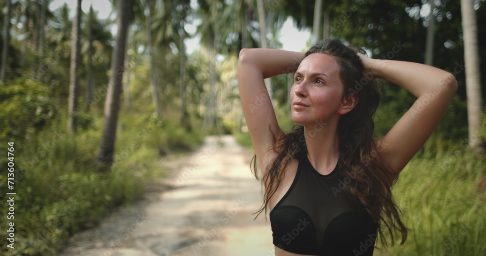 Woman close up portrait enjoy tropical forest walk in sunny day. Hiking trail and green coconuts. Beautiful path among large palm trees. Outdoor lifestyle travel, summer holiday vacation