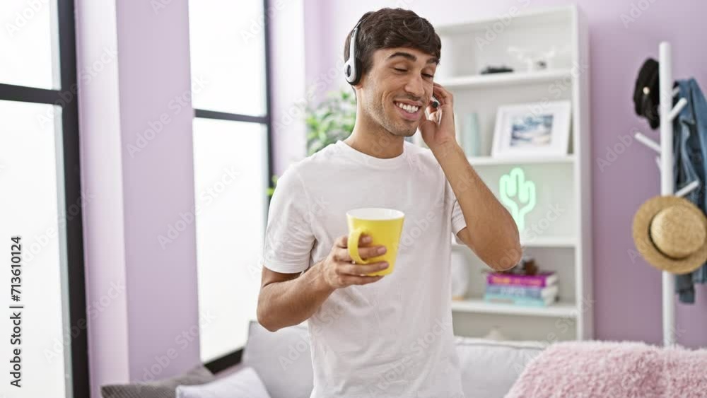 Smiling young hispanic man happily teleworking at home - agent for a call center, hands-free call gadget on, savoring coffee in the living room Smiling young hispanic man happily teleworking at home - agent for a call center, hands-free call gadget on, savoring coffee in the living room