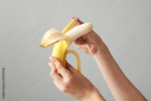 Young woman peeling banana on light background, closeup. Sex concept photo