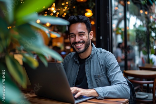 Smiling young Latin business man using laptop sitting outdoor. Happy guy student or professional looking away in city cafe elearning, hybrid working, searching job online thinking of digital solution photo