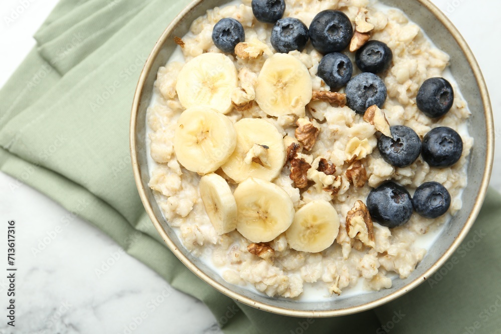 Tasty oatmeal with banana, blueberries, walnuts and milk served in bowl on white marble table, top view Tasty oatmeal with banana, blueberries, walnuts and milk served in bowl on white marble table, top view