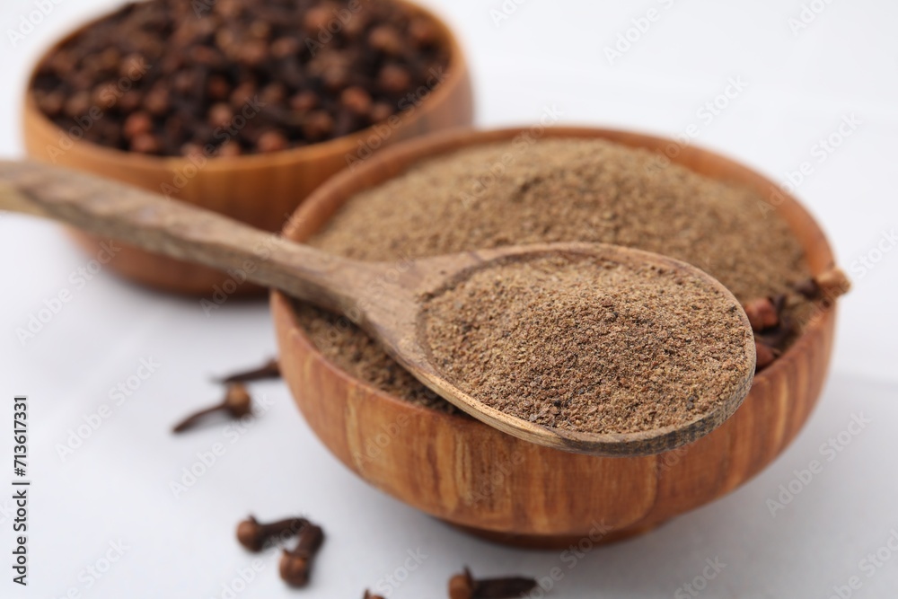 Aromatic clove powder in bowl, dried buds and spoon on white table, closeup Aromatic clove powder in bowl, dried buds and spoon on white table, closeup