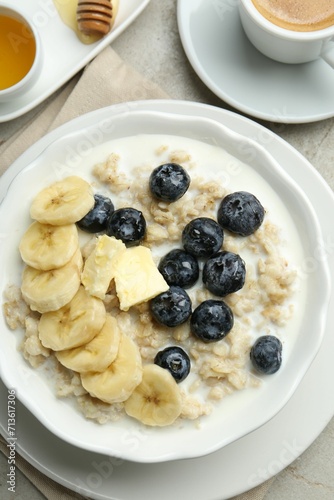 Tasty oatmeal with banana, blueberries, butter and milk served in bowl on light grey table, flat lay