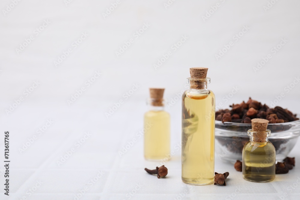 Clove oil in bottles and bowl with dried buds on white tiled table, space for text Clove oil in bottles and bowl with dried buds on white tiled table, space for text