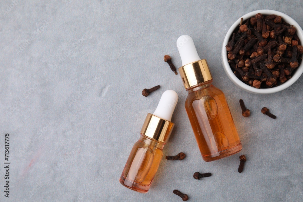 Clove oil in bottles and dried buds on grey table, flat lay. Space for text