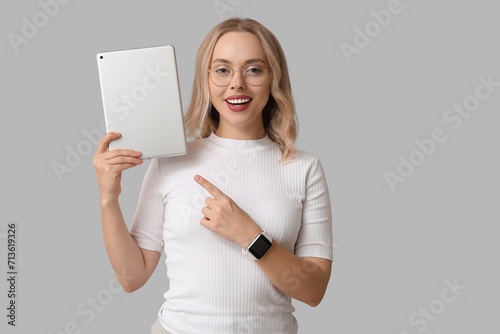 Pretty young woman with modern tablet computer on grey background