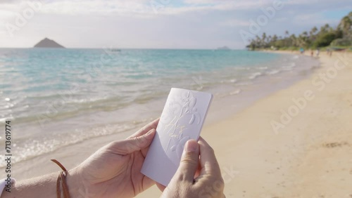 Unrecognizable groom opens pastel blue vow book to read outloud his vows to bride at tropical beach wedding ceremony. Closeup shot male hands holding embossed vow book with vow. Elopement background photo