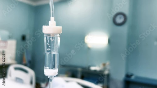 Drip chamber in an IV hangs on a medical infusion stand against the background of blurred medical beds in a clinic ward. Intravenous injections, medical care. Recovering patient in a hospital. Closeup photo