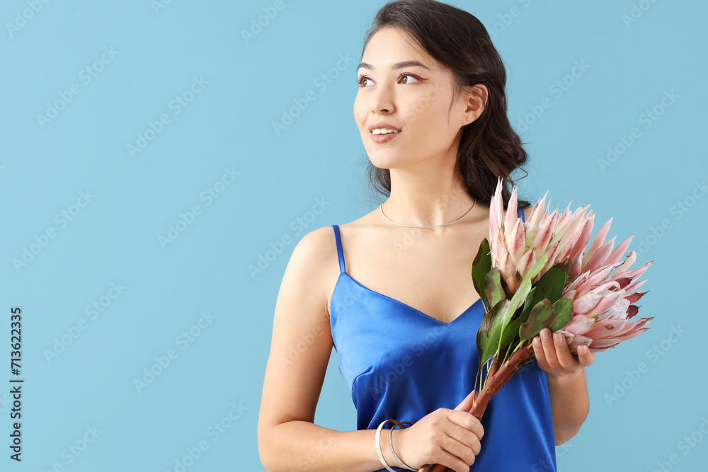 Young Asian woman with beautiful protea flowers on blue background Young Asian woman with beautiful protea flowers on blue background