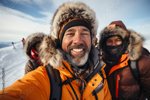 Group of young tourists taking selfie against the backdrop of snowy mountain tops. Cheerful diverse travelers in winter outwear spend vacation together hiking and skiing.