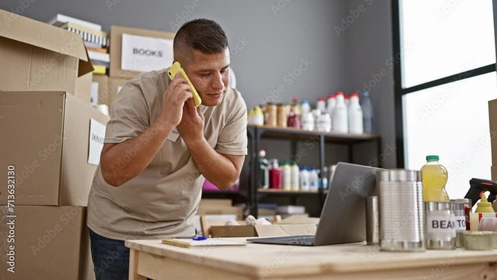 Energetic young latin man volunteering, talking on his smartphone and jotting notes in a heartwarming charity center Energetic young latin man volunteering, talking on his smartphone and jotting notes in a heartwarming charity center