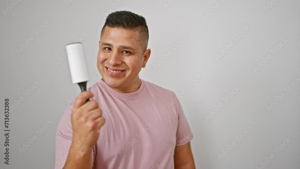 Smiling young latin man confidently uses roll stick to clean pet hair off fabric, standing isolated against a white background Smiling young latin man confidently uses roll stick to clean pet hair off fabric, standing isolated against a white background