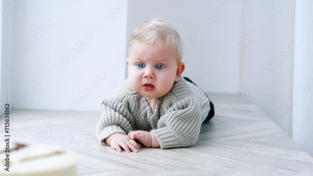 Lovely blond baby in grey sweater lies on his belly. Infant tries to crawl to the cake standing in front of him. Lovely blond baby in grey sweater lies on his belly. Infant tries to crawl to the cake standing in front of him.