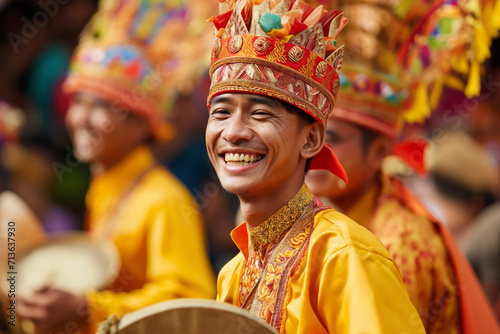 A man in traditional Balinese attire laughs joyfully, wearing a colorful headdress during a festive event. photo