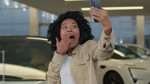 Joyful girl African American woman blogger taking selfie photo in car showroom buying new auto in dealership salon happy cheerful client buyer blogging with smartphone advertising automobile vehicle
