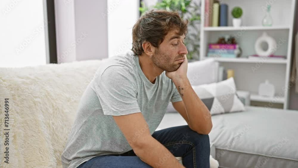 Bored, tired-looking young man, sitting on his cozy home sofa, arms crossed, pondering his depression problem with a gloomy expression. Bored, tired-looking young man, sitting on his cozy home sofa, arms crossed, pondering his depression problem with a gloomy expression.