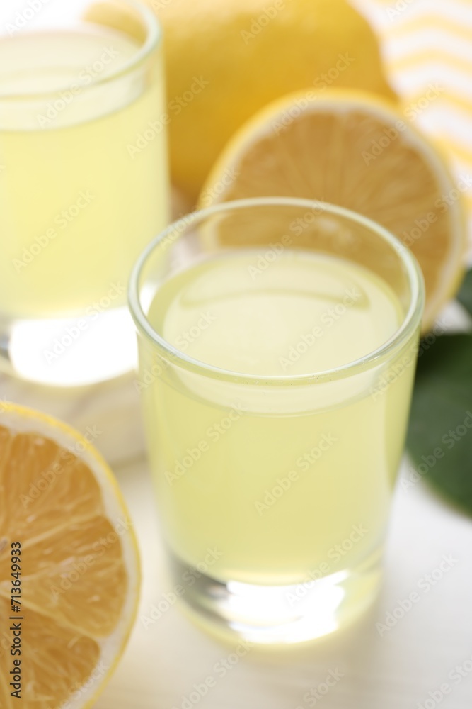 Shot glasses with tasty limoncello liqueur and lemons on table, closeup Shot glasses with tasty limoncello liqueur and lemons on table, closeup