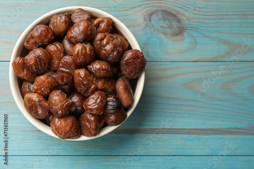 Roasted edible sweet chestnuts in bowl on light blue wooden table, top view. Space for text photo