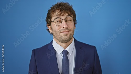 Cheerful young man, confident and thinking, in fashionable business suit, looking away to the side with a happy, smiling face. over blue, isolated background, he's a smart look. photo