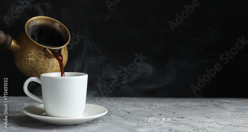Turkish coffee. Pouring freshly brewed beverage from cezve into cup on grey table. Banner design with space for text photo
