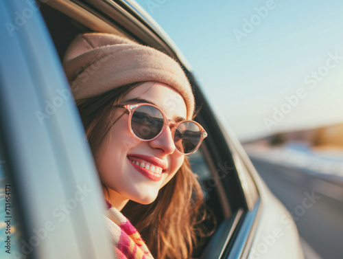 A happy woman in glasses looks out through the window of a moving car © kura