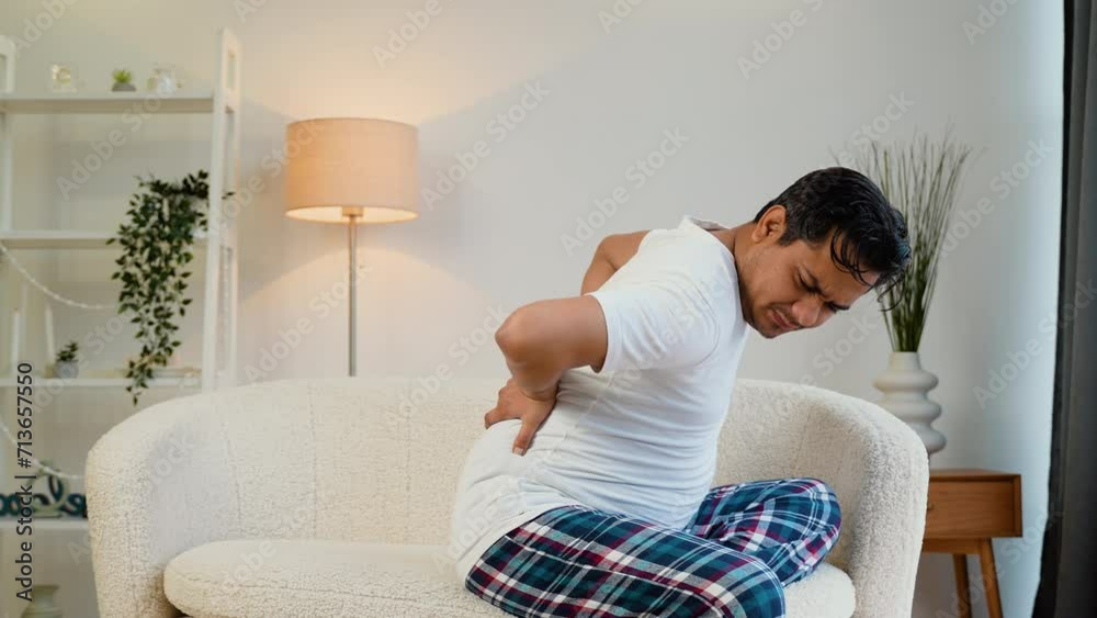 Indian man suffering from backache while sitting on sofa at home Indian man suffering from backache while sitting on sofa at home