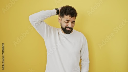 Pensive young man in yellow, doubting and unsure, scratching his head in a puzzled stance. surrounded by an isolated background, his uncertainty is clear as he grapples with questions. photo