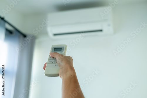 A woman's hand presses the air conditioner remote and points at the air conditioner to operate it.