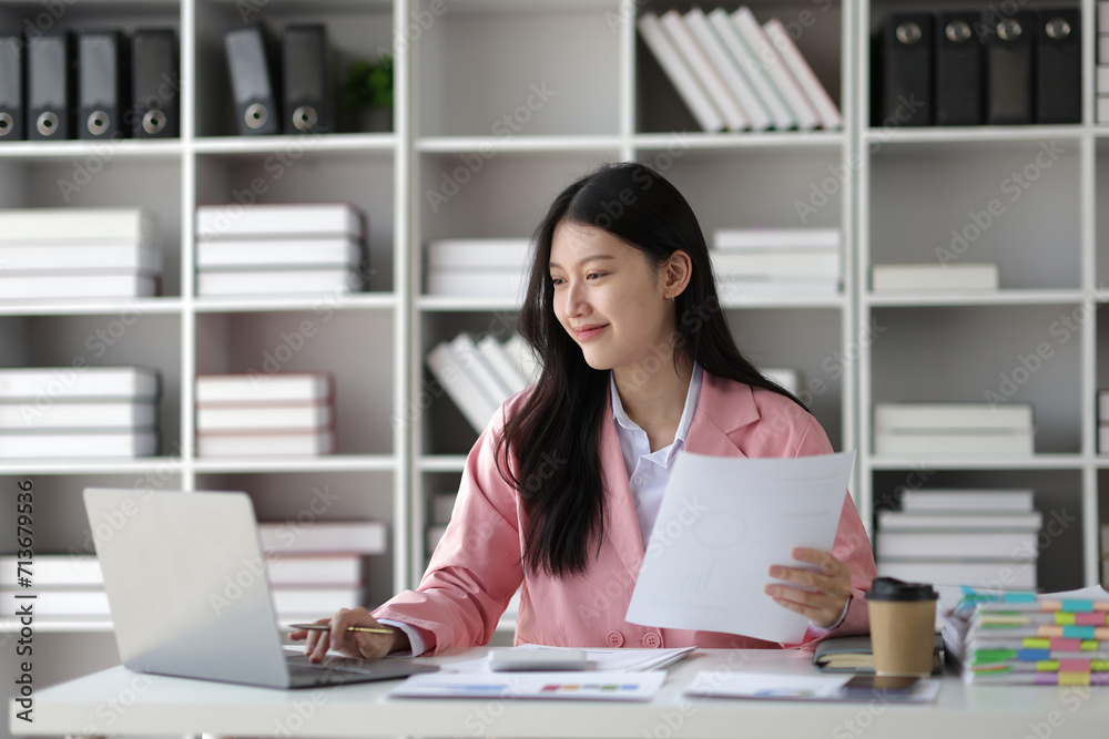 © Kainnika - Young beautiful asian businesswoman working with laptop and paperwork on desk in office.