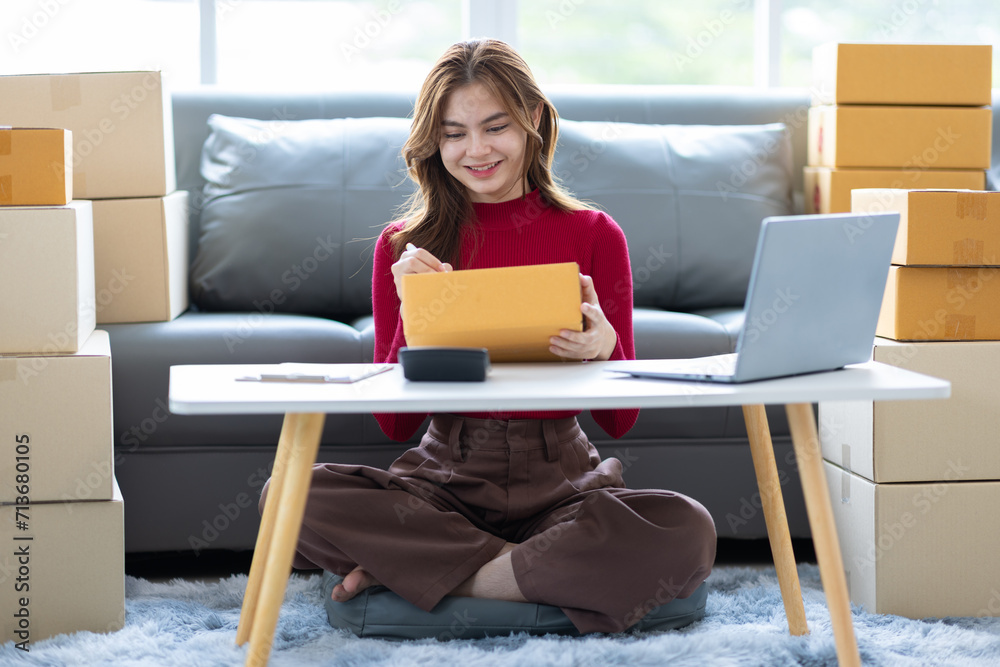 Young Asian woman starting a small online shopping business from home checking internet orders on her laptop. Young Asian woman starting a small online shopping business from home checking internet orders on her laptop.