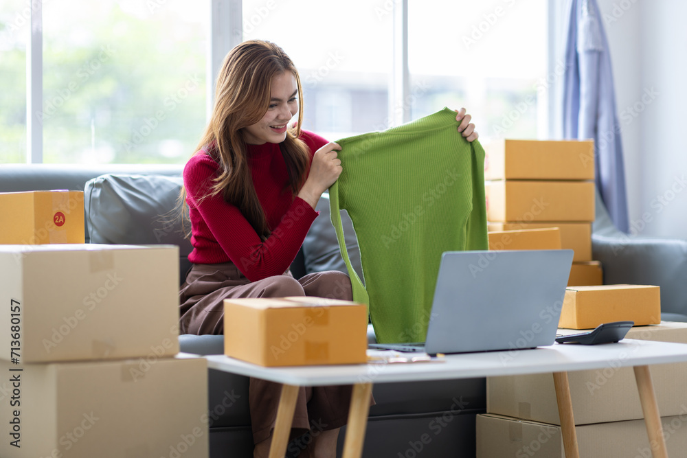 Young Asian woman starting a small online shopping business from home checking internet orders on her laptop. Young Asian woman starting a small online shopping business from home checking internet orders on her laptop.