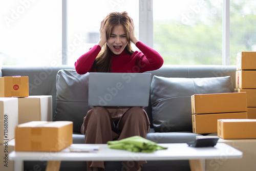 A woman is surprised while looking at the plan of the sofa. Young Asian woman starting a small online shopping business from home checking internet orders on her laptop.