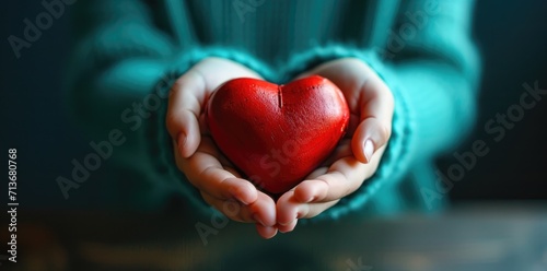 Close-up hand holding red heart concept on green background.