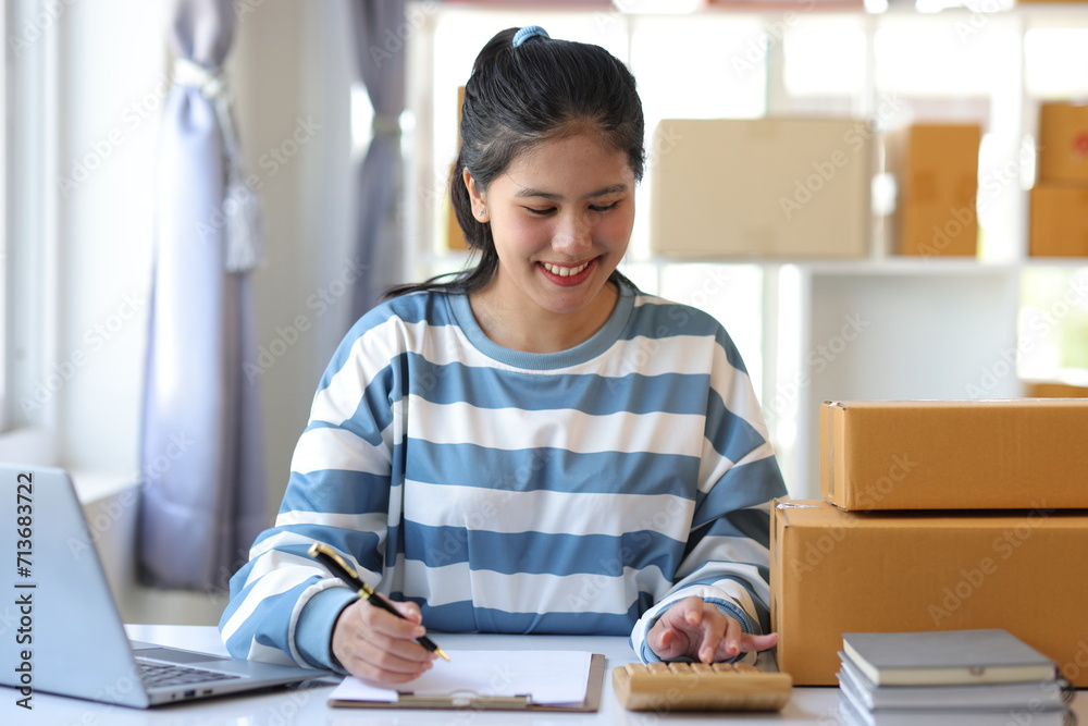 Young Asian woman starts an online shopping business at home using a calculator to calculate costs and profits. Young Asian woman starts an online shopping business at home using a calculator to calculate costs and profits.