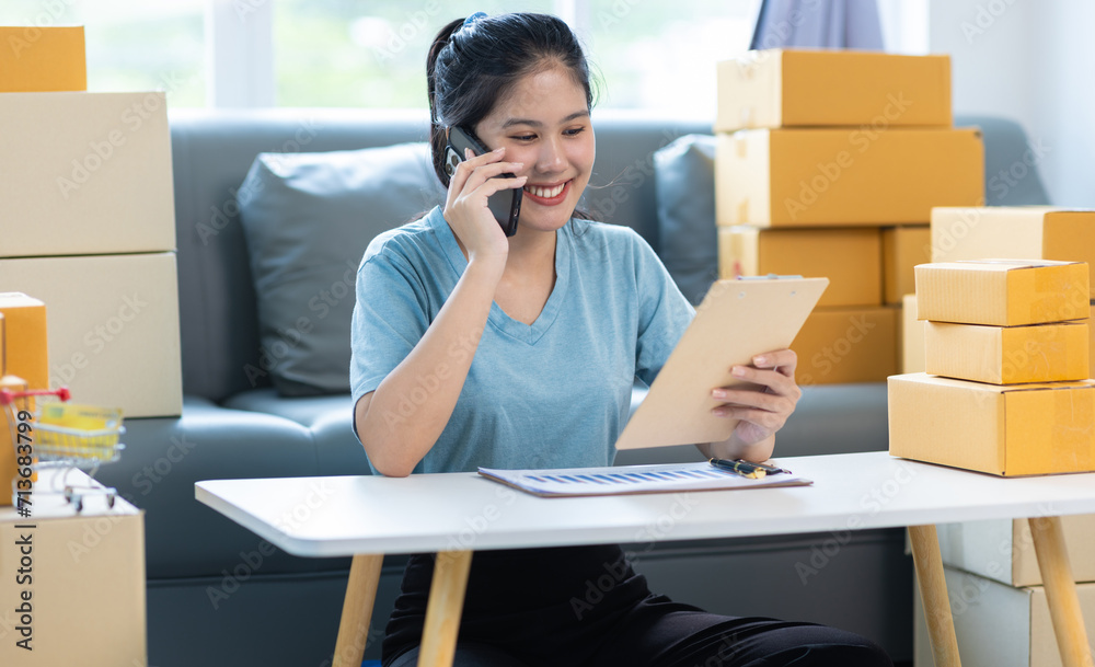 Young Asian woman starting an online selling business at home using mobile phone is checking online messages and calling customers. Young Asian woman starting an online selling business at home using mobile phone is checking online messages and calling customers.