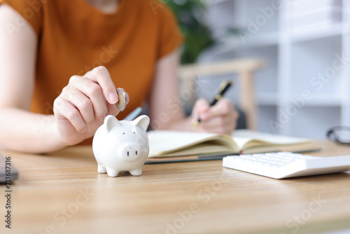 Asian woman putting money into piggy bank at home. Savings, Accounting and Financial Planning photo