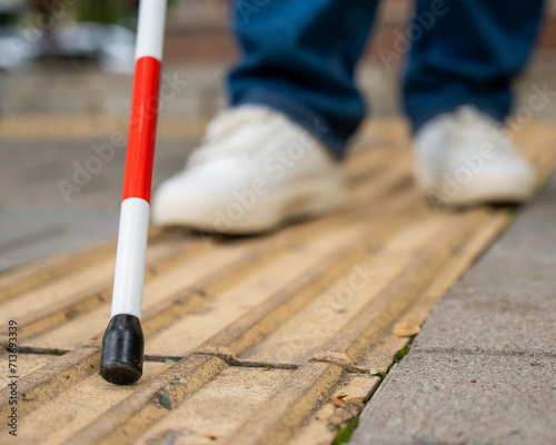 A blind woman walks on the street on tactile yellow tiles. Focus on the tactile cane. 