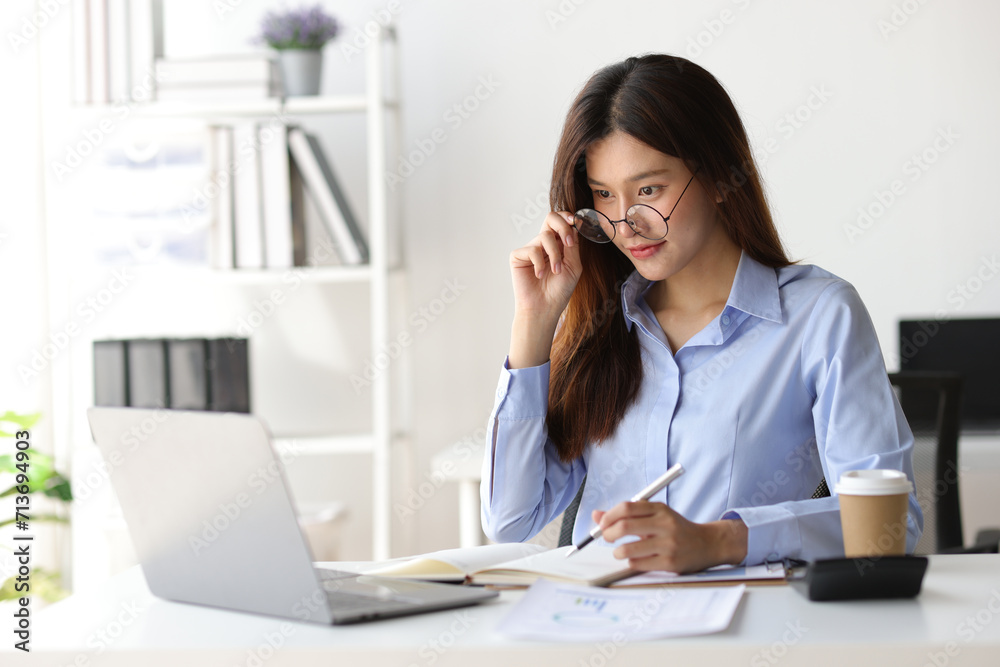 Businesswoman working on financial documents on the desk in the office is writing notes and calculating income and expenses. Businesswoman working on financial documents on the desk in the office is writing notes and calculating income and expenses.