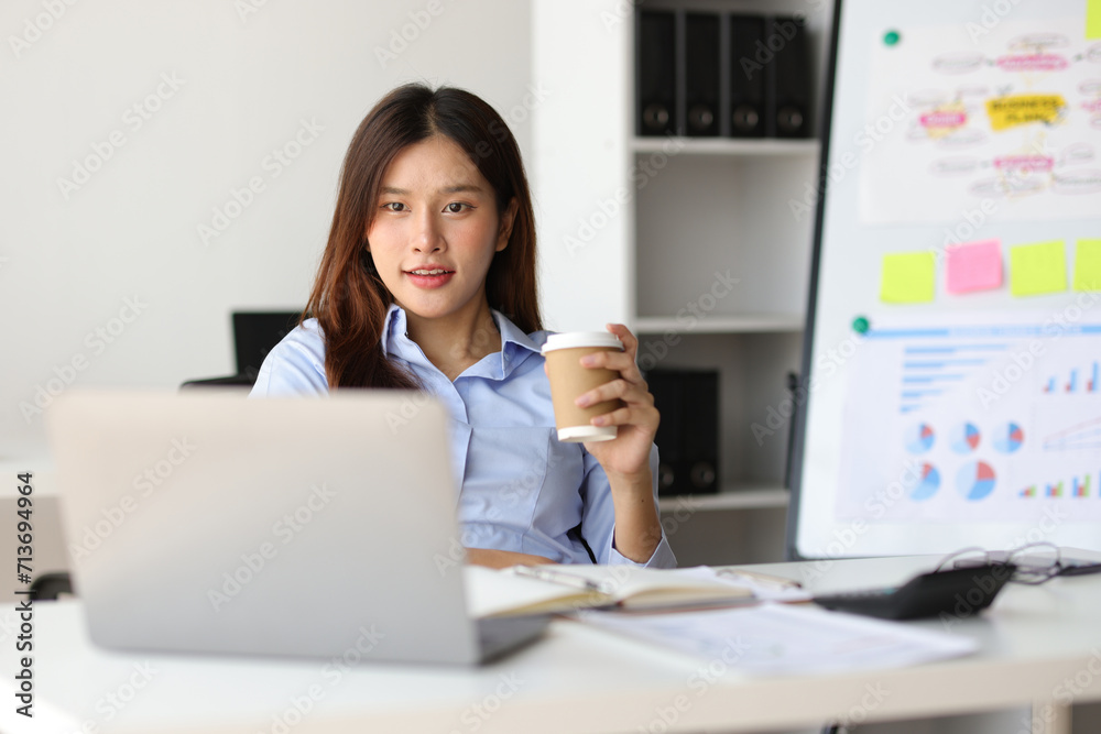Portrait of a charming Asian businesswoman in casual clothes drinking hot coffee and relaxing during a break in the office. Portrait of a charming Asian businesswoman in casual clothes drinking hot coffee and relaxing during a break in the office.