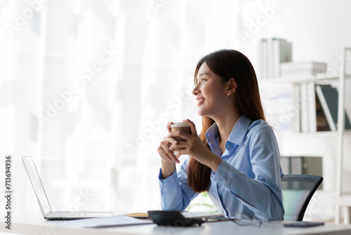 Portrait of a charming Asian businesswoman in casual clothes drinking hot coffee and relaxing during a break in the office.