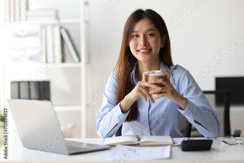 Portrait of a charming Asian businesswoman in casual clothes drinking hot coffee and relaxing during a break in the office.